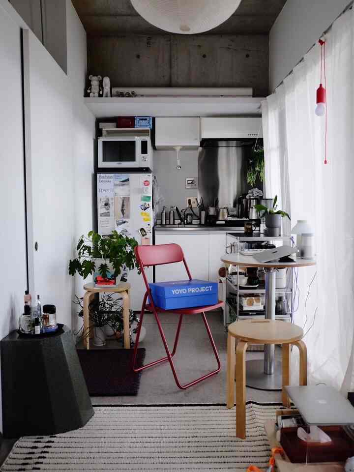 White and red toned studio kitchen space featuring minimal furniture and plants with a modern atmosphere