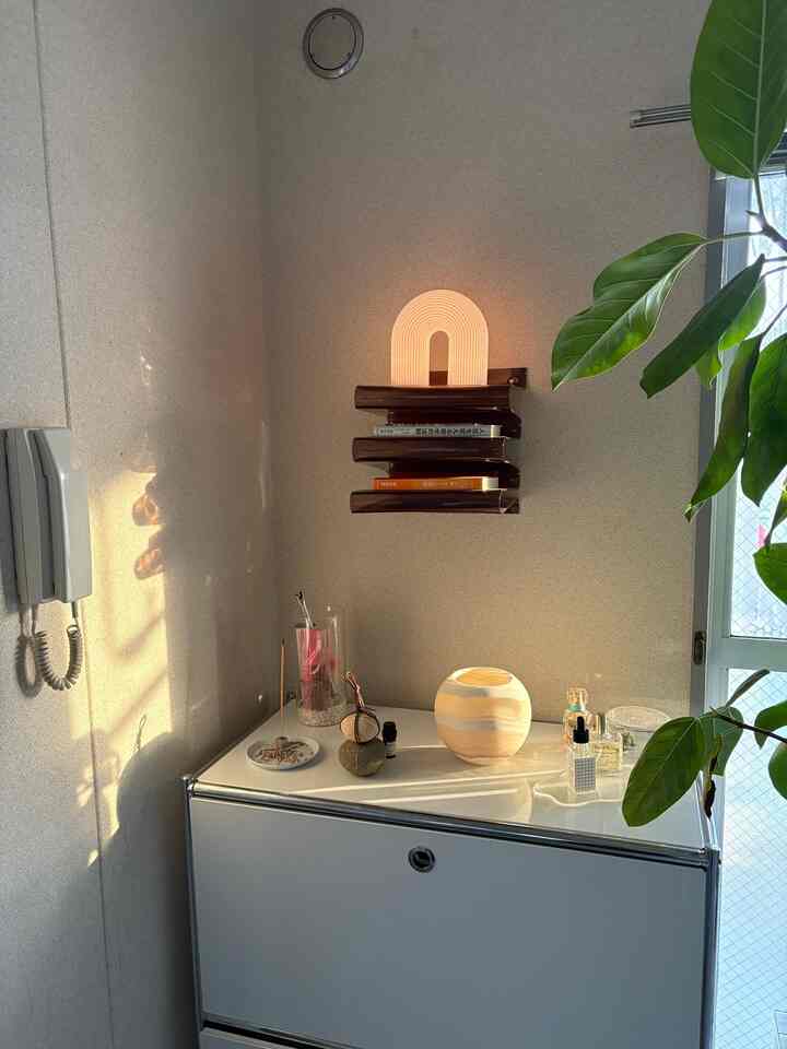 白を基調とした玄関スペース、シンプルなサイドボードの上に植物と照明、香りのアイテムが配置されたミニマルで雰囲気のあるインテリア