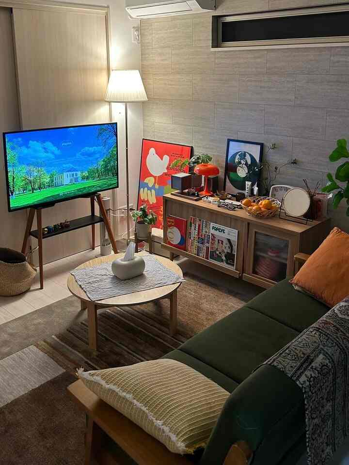 ナチュラルトーンのリビング、緑のソファと丸いコーヒーテーブル、テレビ台とフロアランプが配置された雰囲気のあるインテリア