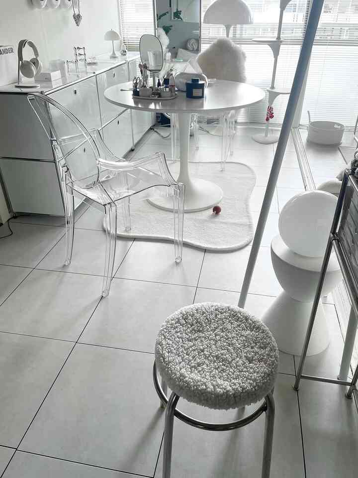 ホワイトとグレーのトーンのダイニングルーム、透明な椅子とラグが配置された洗練されたミニマルモダンな空間