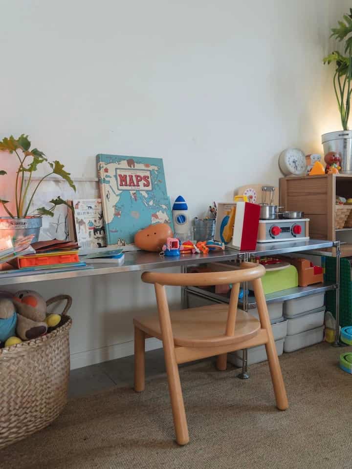 ナチュラルカラーとベージュの子供部屋、木製の椅子とデスク、おもちゃ収納とステンレスの棚が配置された雰囲気のあるインテリア