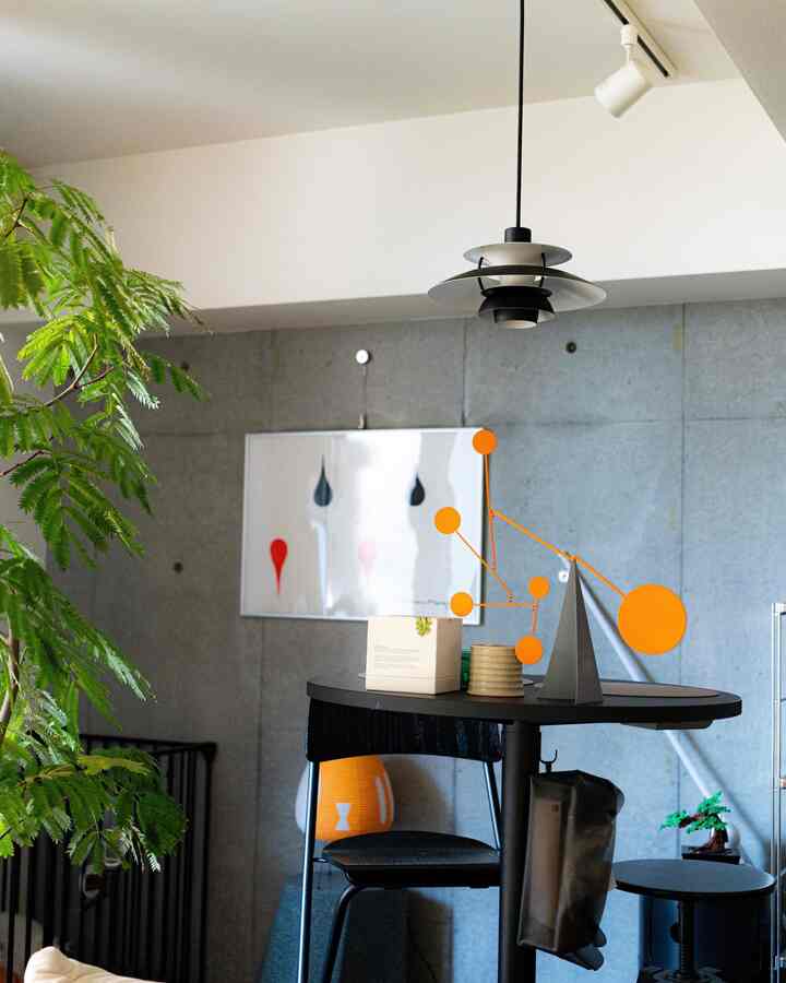 グレーのコンクリート壁と黒の丸テーブル、オレンジのモビールが配されたミッドセンチュリーモダンのダイニング空間