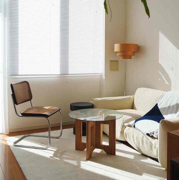 Bright white and wood tone studio living room with a low sofa, round wooden coffee table, and window blinds creating a cozy atmosphere