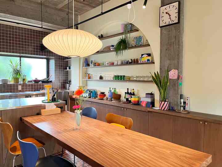 Natural-toned dining room with wooden dining table, various dining chairs, pendant light, and kitchen harmoniously arranged