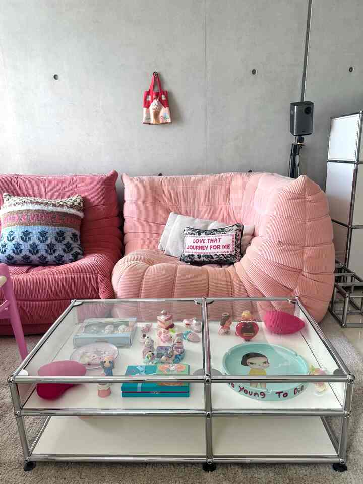Modern living room with pink sectional sofa and glass-top low table against gray concrete wall background
