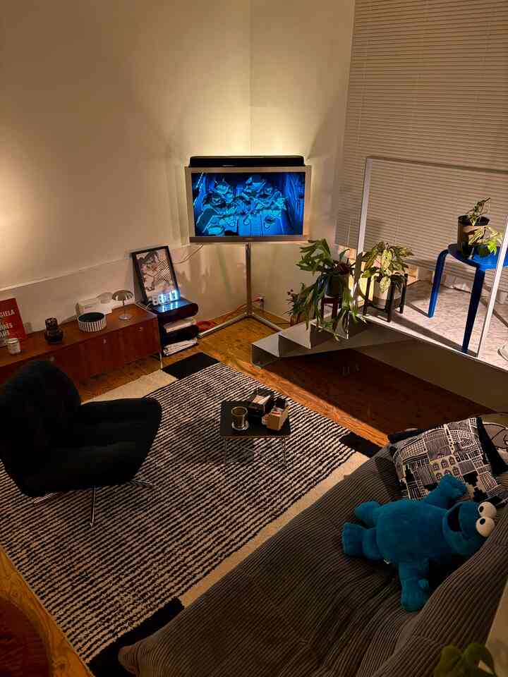 Monotone and natural toned living room featuring mid-century modern sofa, armchair, TV stand, and plants, creating a cozy atmosphere