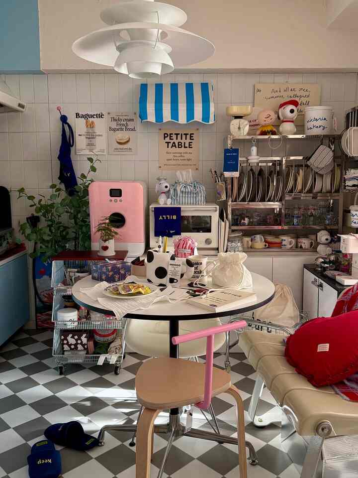 白とピンクの色調が特徴的なダイニング、丸いダイニングテーブルと個性的な椅子、ソファ、キッチン機器が配置された雰囲気のあるインテリア