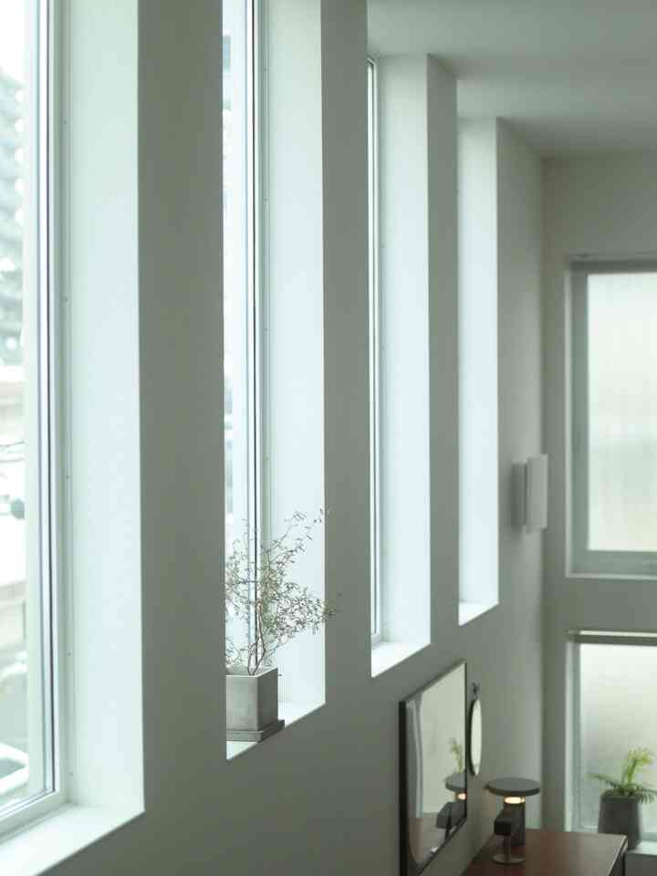 Bright white narrow veranda with tall windows, plants, and a table lamp creating a natural and minimal atmosphere