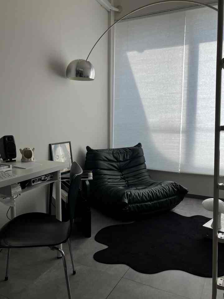 モノトーン調のコンパクトなリビング、シルバーのアーチ型フロアランプと黒のレザーアームチェアが配置された印象的な空間