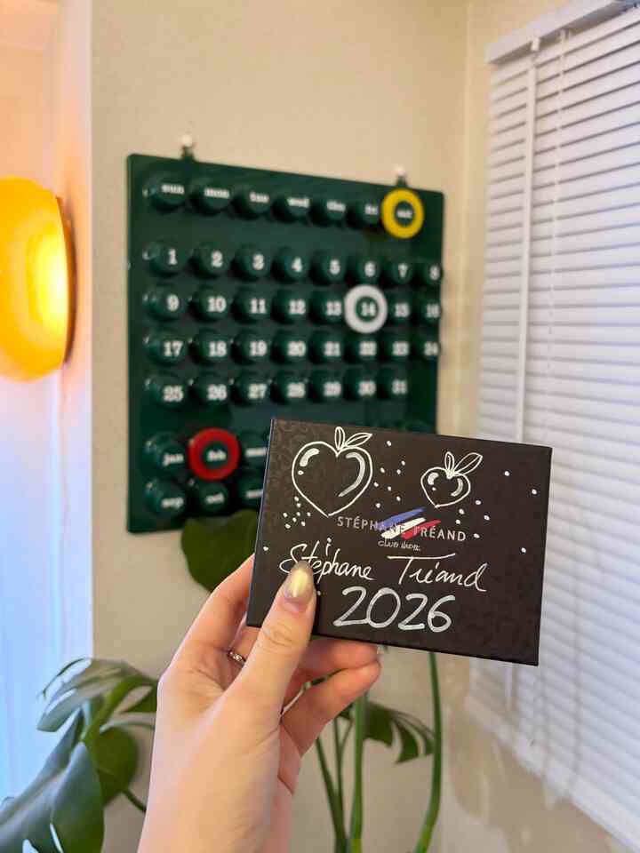 ベージュの壁にミッドセンチュリーモダンスタイルの壁掛けカレンダーがあり、黄色の壁照明と植物が配置された二人暮らしの印象的なインテリア