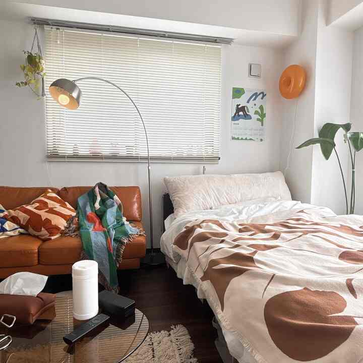 Brown and white toned 1K bedroom with leather sofa, large bed, plants, creating a warm cozy atmosphere