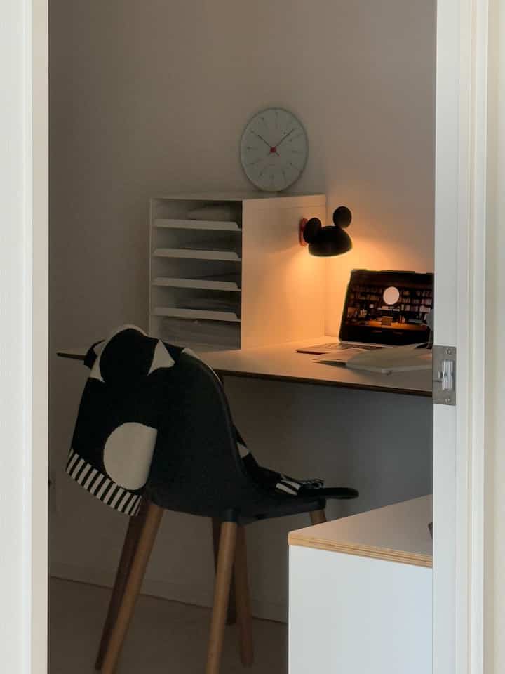White and black toned studio apartment home office featuring a simple desk, chair, and Mickey Mouse table lamp creating cozy atmosphere