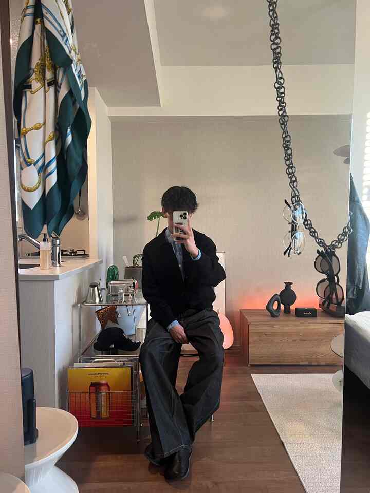 A simple modern living room with white walls and brown wood tone furniture featuring a frameless full-length mirror and stool