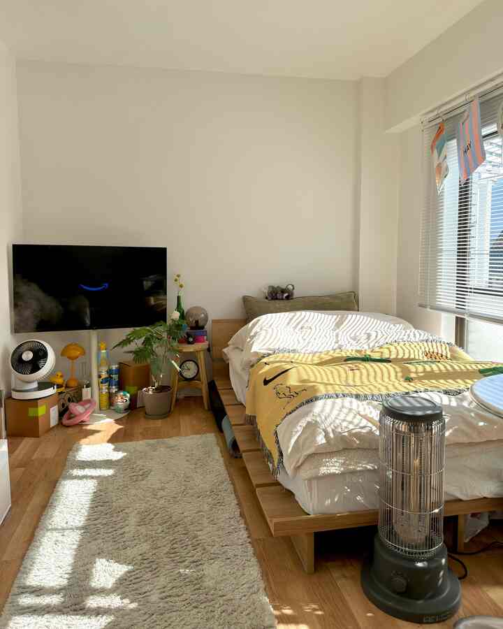 白い壁と木目調の床の一人暮らしの寝室、木製のベッドとスツールが配置された温かみのある空間