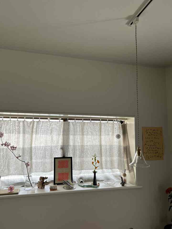 ベージュのカーテンと白い壁、透明なガラスのペンダントライトがあるワンルームのインテリア小物配置された空間