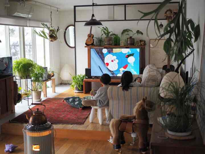 ブルーとブラウンの色調のリビング、子供とソファ、多様な植物が配置された温かみのある空間