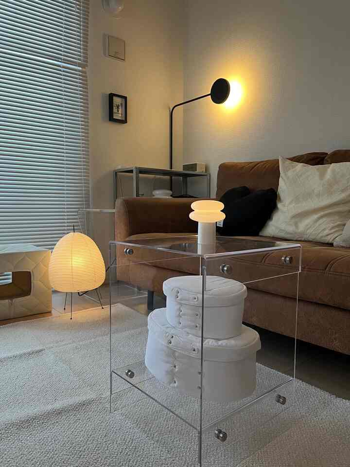 透明なアクリルのサイドテーブルとブラウンソファ、白いラグとクッションが配置された1LDKのモダンなリビング空間