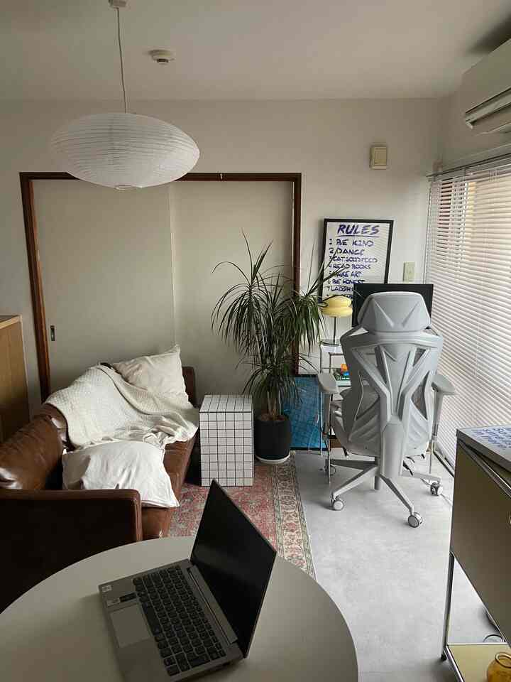 White and brown toned 1DK single household living space featuring brown leather sofa and remote work desk with an overall cozy atmosphere
