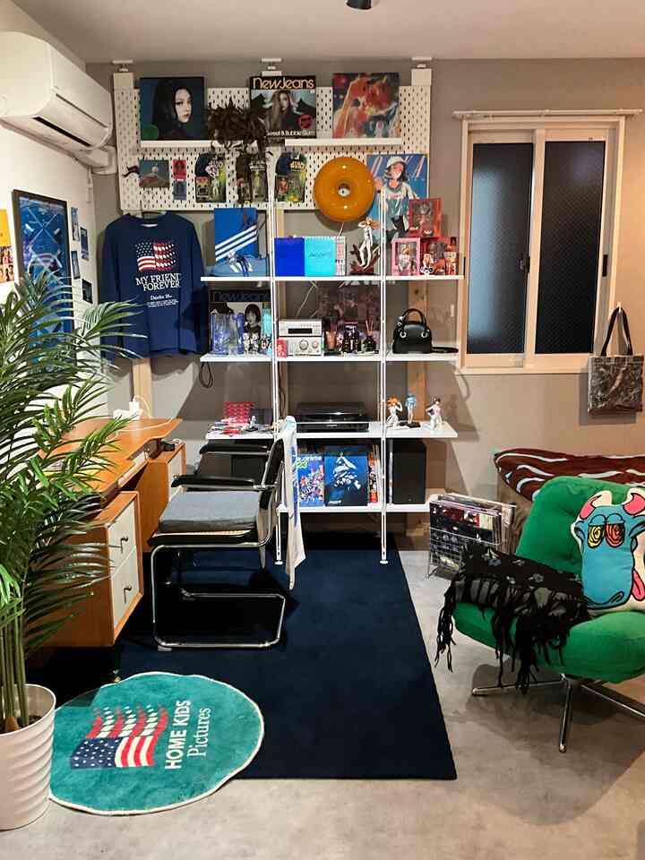 グレーの壁と白い棚が配された小さなリビング兼ホームオフィス、緑のソファと木製家具がある居心地の良い空間