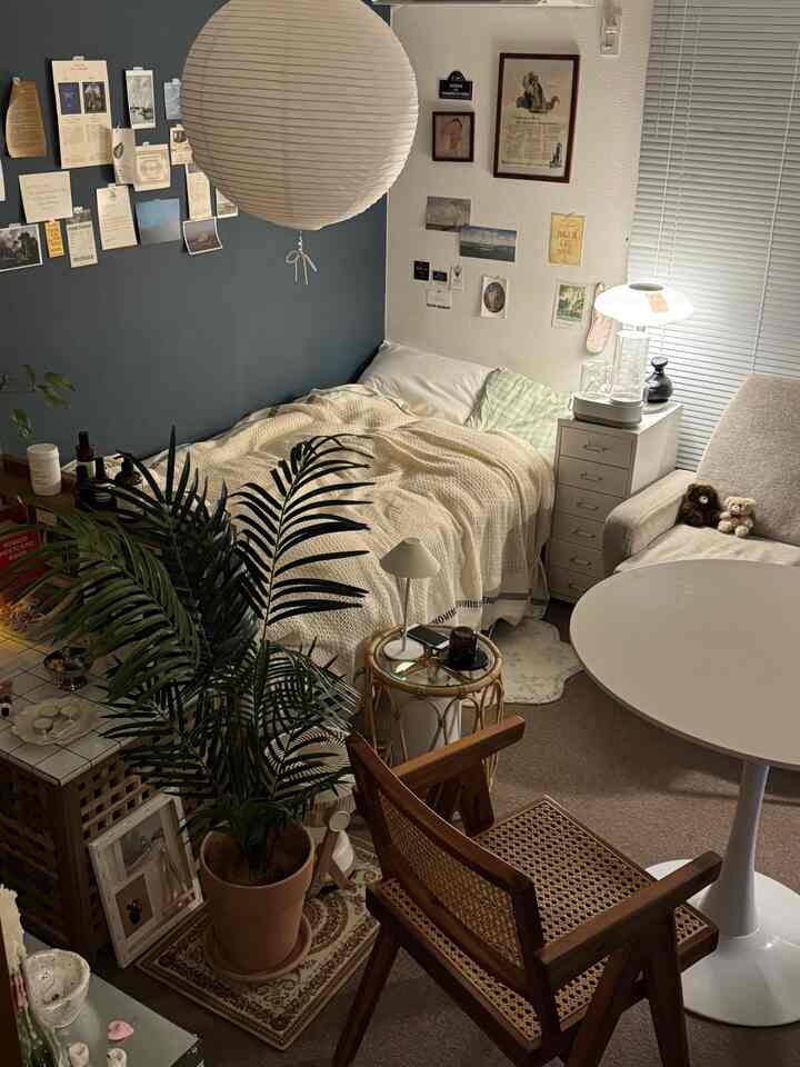 ナチュラルカラーと白を基調とした7畳の1Kワンルーム、ベッド横にナイトテーブルとラタンチェア、丸テーブルが配置された雰囲気のある空間