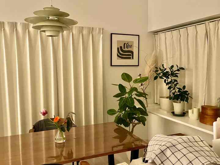 クリーム色のカーテンと木製のダイニングテーブル、ペンダントライトが配置されたナチュラルモダンな北欧ダイニングルームの空間