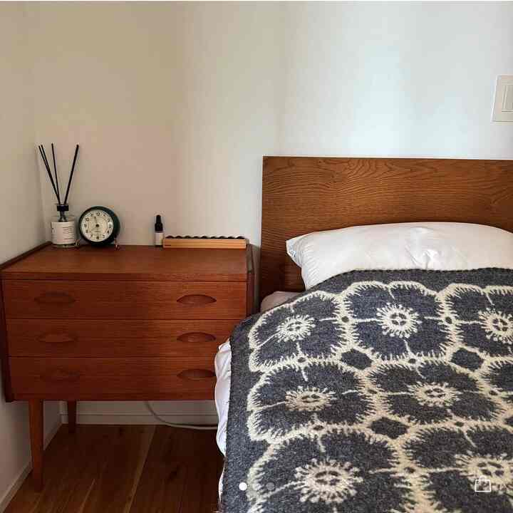 白い壁とブラウンの木製家具が配置されたミニマルな北欧風寝室、グレーの柄のスローがベッドに掛けられている