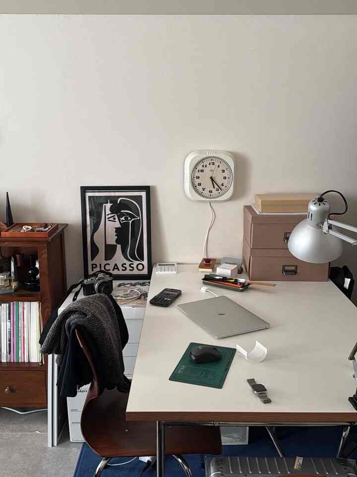 白と茶色のトーンのワークスペース、机と椅子、壁掛け時計、ピカソのポスターが配置された清潔感のある書斎のインテリア