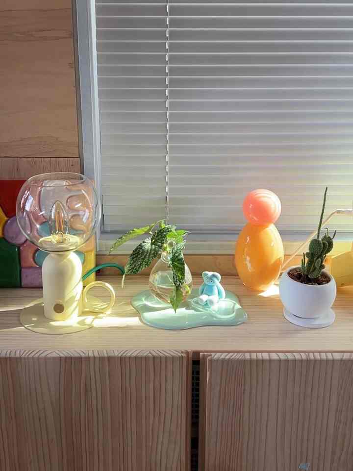A Korean interior space featuring warm wood tones and natural light, with plants and lighting accessories on a serene shelf