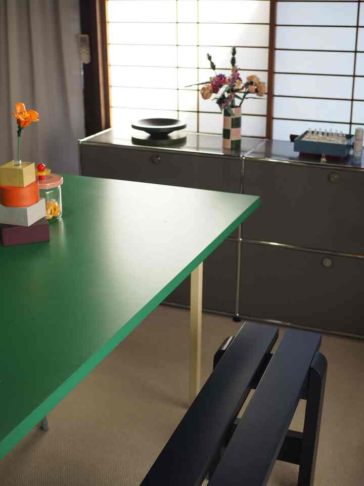 Modern mid-century living room with brown window frames and green table, featuring simple decor and a sideboard