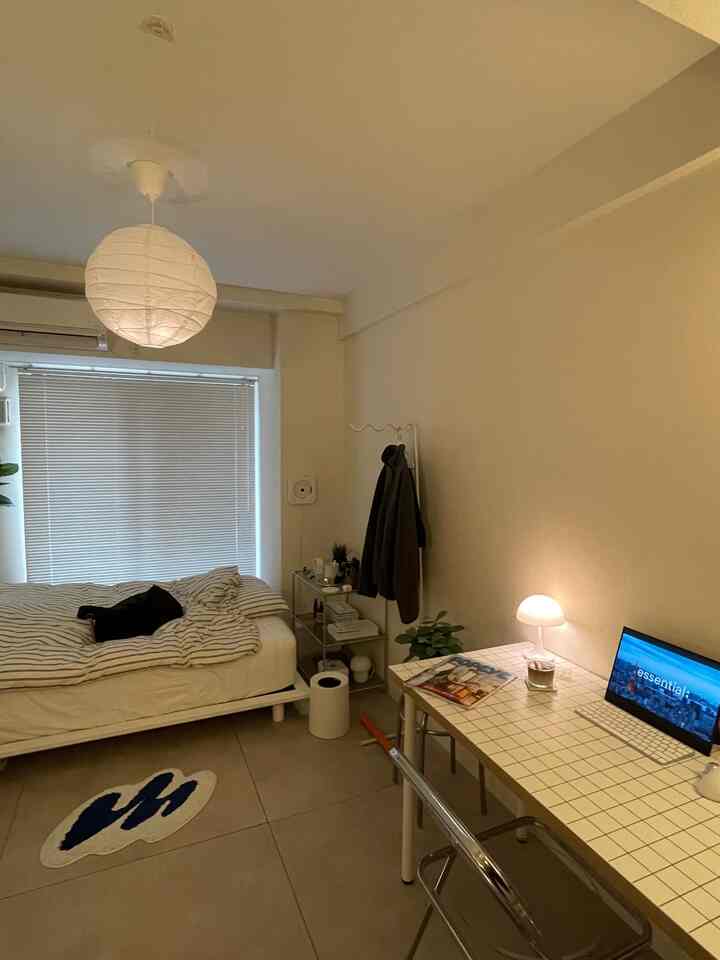 暖かい白を基調とした一人暮らしの寝室、モダンなデスクとテーブルランプが配置された雰囲気のある空間