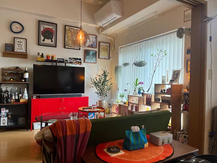 レッドの家具と多様な植物が配置された、ヴィンテージ感のある雰囲気のある散らかったリビング