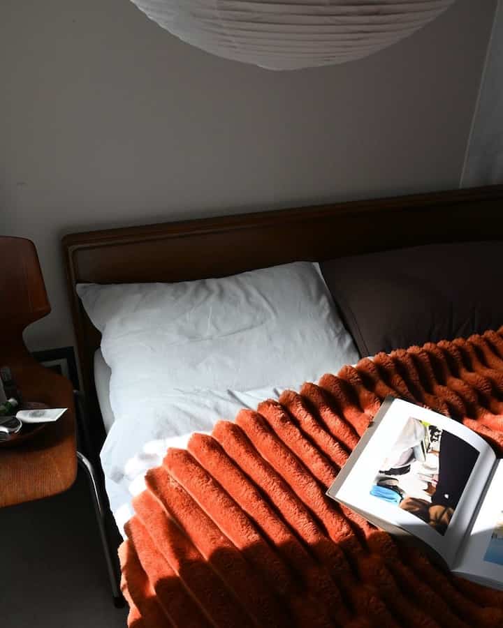 ブラウンの木製ベッドフレームと白い枕、オレンジ色のブランケットが配置された雰囲気のある寝室