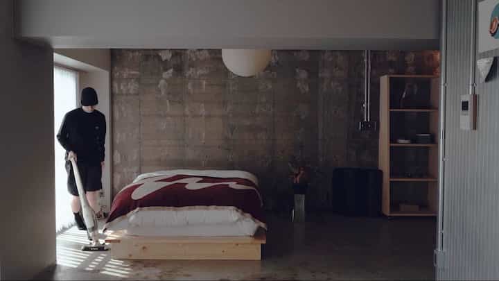 ナチュラルな色調の小さな寝室、中央に木製のプラットフォームベッドと白いペンダントライトが配置されたモダンな空間