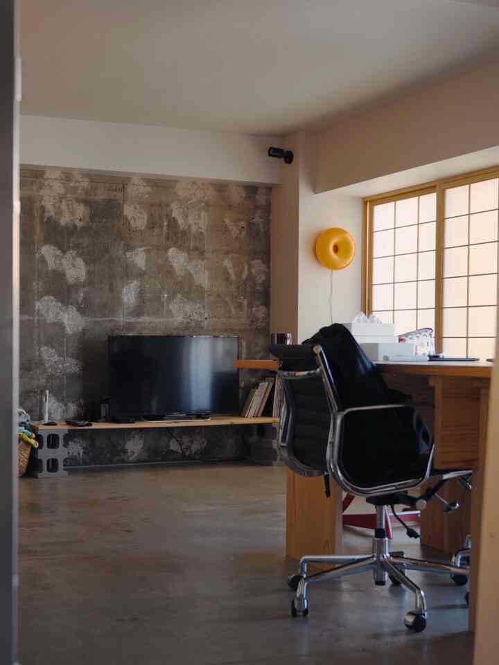 Natural color-toned studio apartment home office with black accents, featuring a concrete wall and Shoji windows creating a harmonious interior