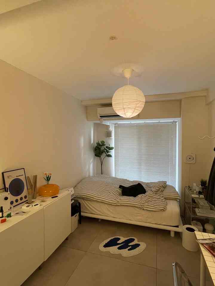 White and beige toned studio bedroom featuring a centrally placed bed and shelving on the left, creating a cozy space