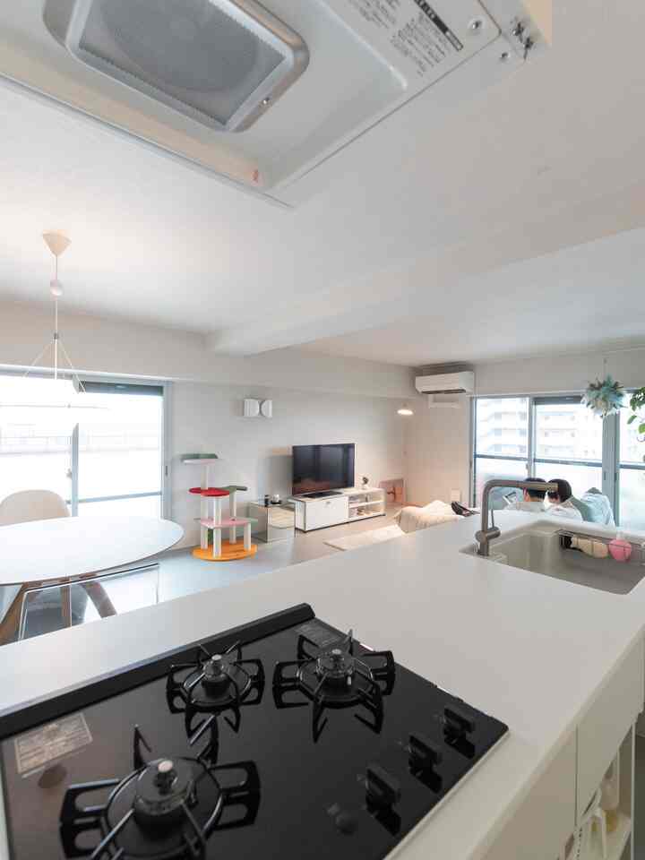 明るいホワイトトーンのキッチンとリビング、キャットタワーと円形ダイニングテーブルが配置されたモダンな二人暮らしの空間