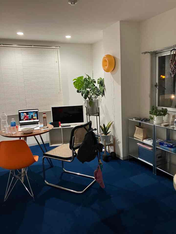 白い壁とネイビーのカーペットが調和する6畳のホームオフィス、丸テーブルとオフィスチェア、観葉植物が配置された落ち着いた空間