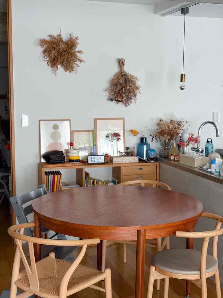 白い壁と木目調の丸テーブル、ドライフラワーの飾りとシンプルなペンダントライトが配置されたヴィンテージダイニングルーム