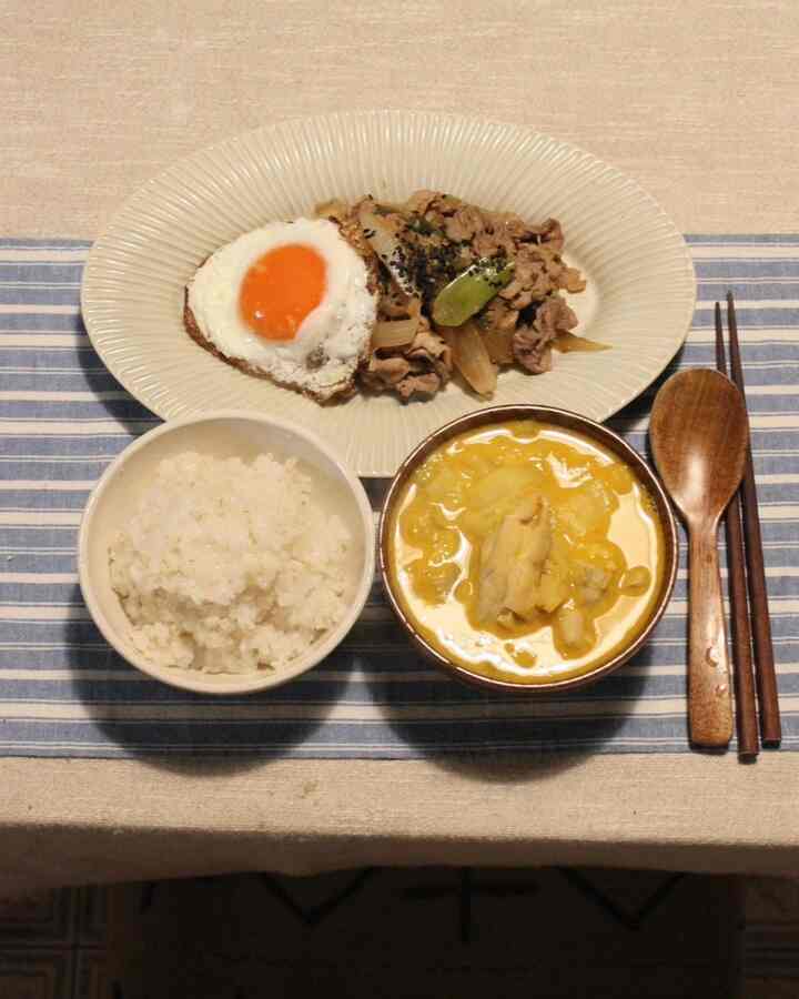 白と茶色のトーンのダイニングテーブルに、ご飯の器、スープの器、目玉焼きと肉がのったオーバル皿、木製のスプーンと箸が置かれた整った夕食のセッティング