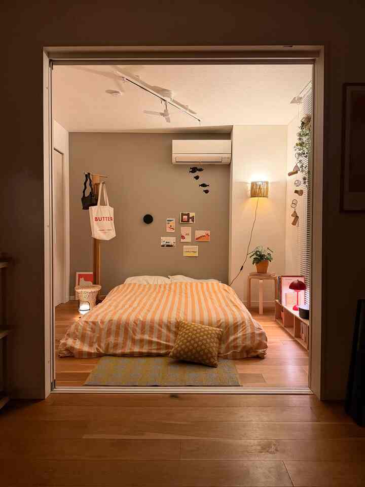 Warm wood tone and white-walled bedroom featuring a centrally placed orange striped bedspread and cushion, creating a cozy atmosphere