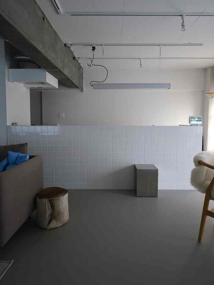 Gray floor and white tiled kitchen in industrial-style dining space featuring brown sofa, side table, and minimalist decor