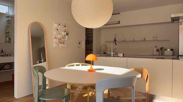 白と木目調のモダンなダイニングルーム、中央に楕円形のテーブルとオレンジのテーブルランプが配置された落ち着いた空間