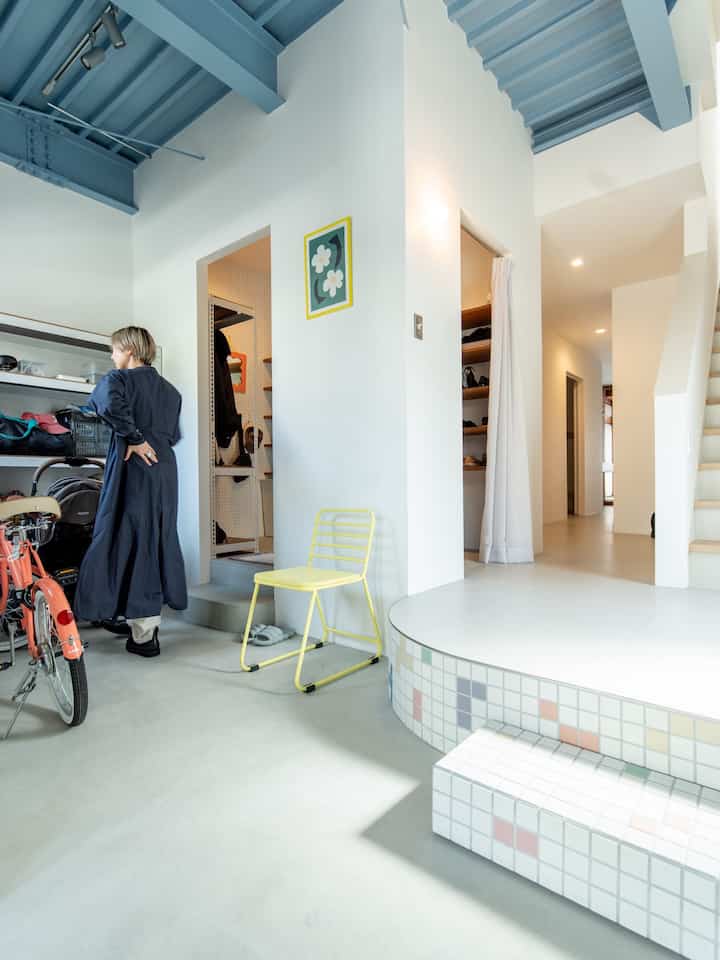 白い壁とスカイブルーの天井が調和するモダンな玄関、黄色い椅子と自転車が配置され、収納アイディアが光る空間