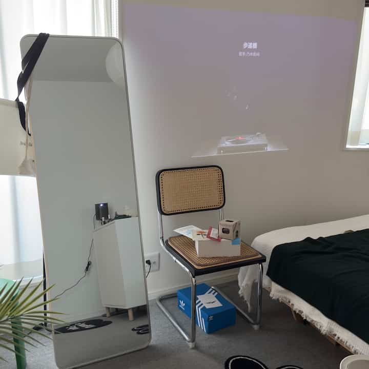 白とベージュのトーンが特徴の寝室、ラタンチェアと大型のスタンドミラーが配置された自然な雰囲気のインテリア