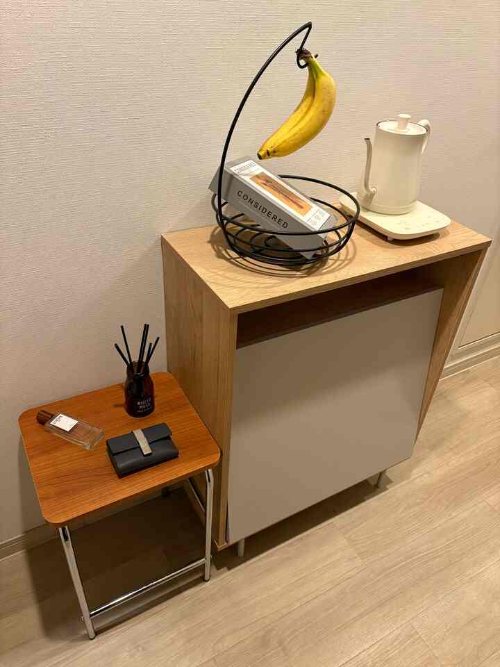 ナチュラルカラーの1K玄関、木製キャビネットとスツールに小物が置かれたシンプルで落ち着いたインテリア