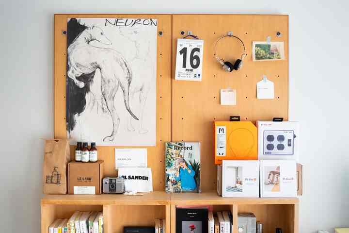 明るい木目調の壁パネルと棚があるシンプルな空間、ポスターやヘッドフォンの製品箱が飾られた雰囲気のあるギャラリーウォール