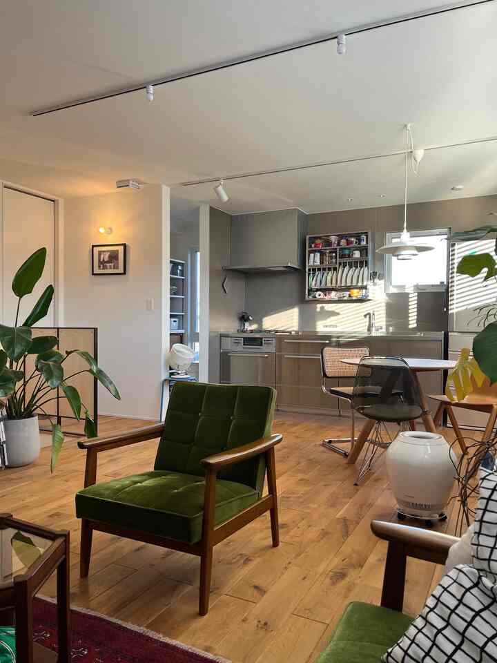 Natural wood tone flooring with green armchairs in living room connected to a stainless steel kitchen with pendant lighting