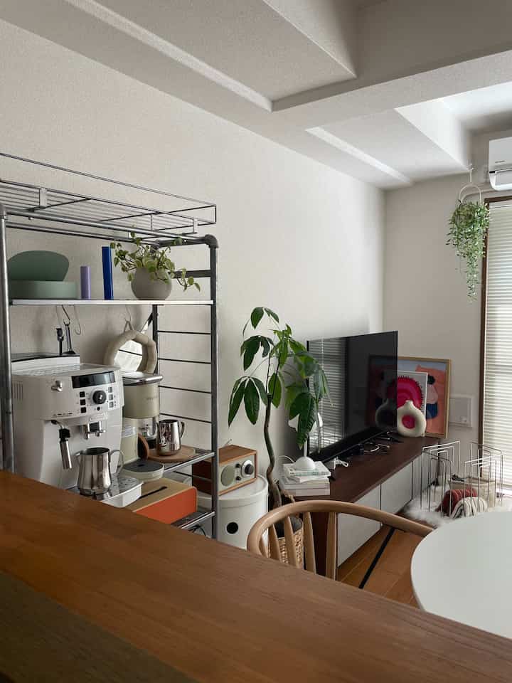 White and wood tone living room featuring metal shelves with coffee machines, TV, and dining chair in a modern and natural atmosphere
