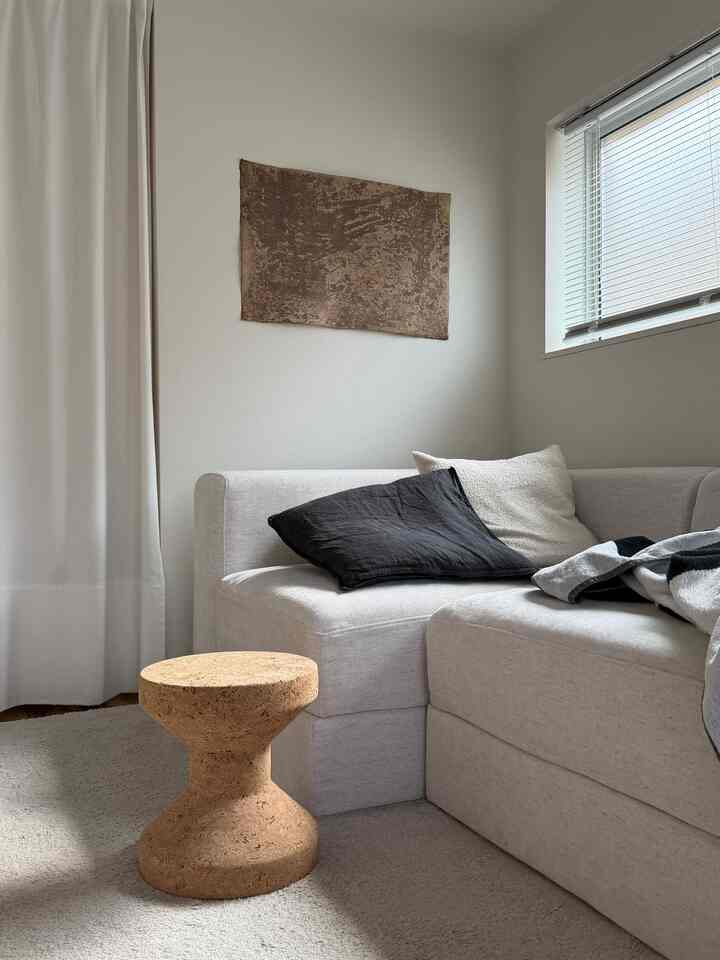 ベージュと白を基調としたリビング、コルク素材のスツールと淡い色合いのソファが配置された落ち着いた雰囲気のインテリア