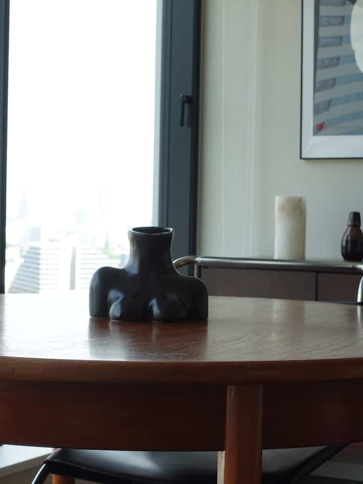 Modern interior space with a dark brown wood tone round table featuring a black sculptural vase